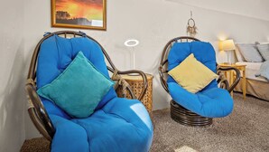 Dos sillones azules con cojines, una mesita redonda, una lámpara y un cuadro de un atardecer en la pared.