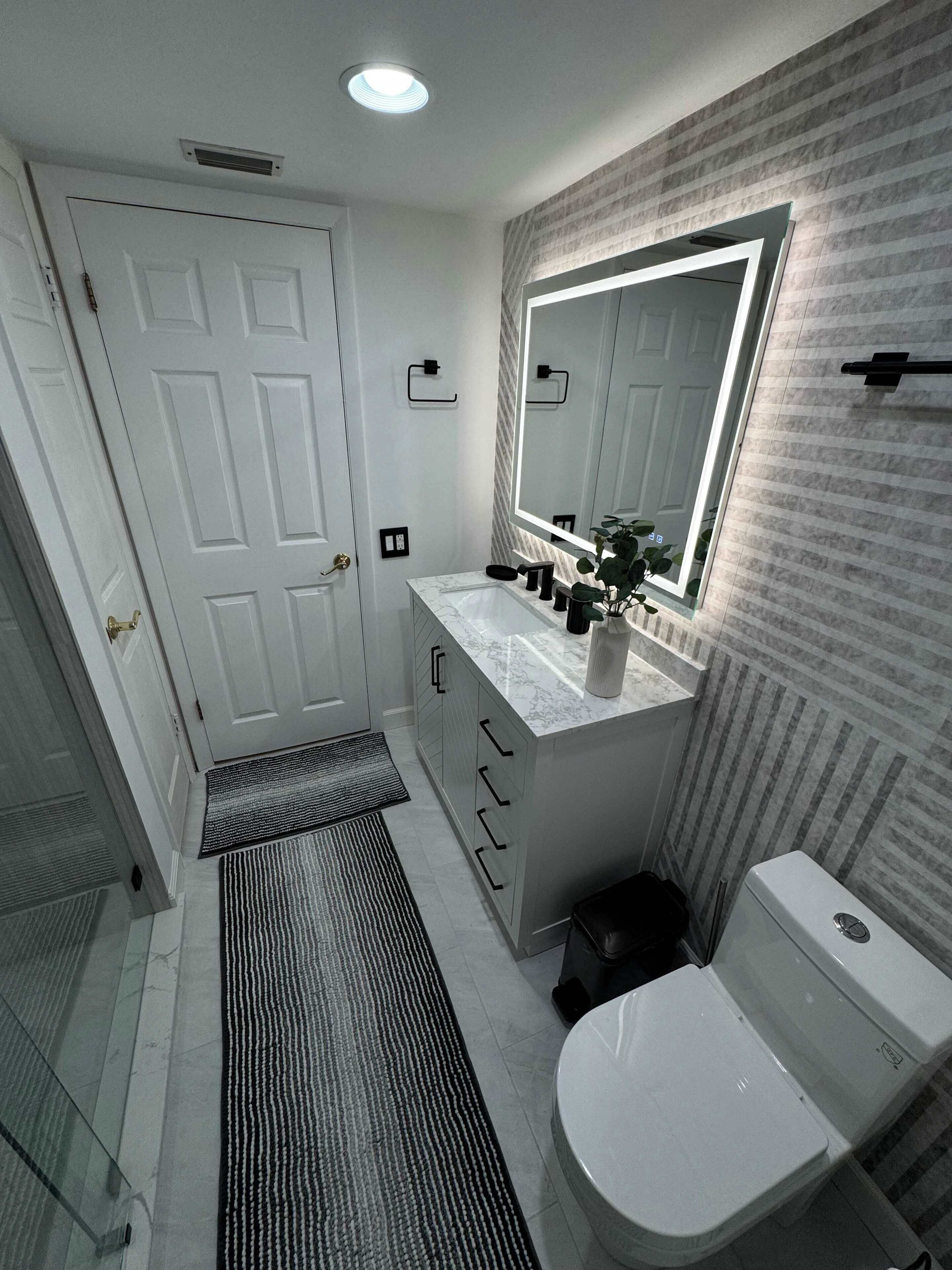A modern bathroom with a white toilet, a marble sink, and a large mirror.