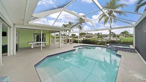 A covered outdoor swimming pool with a clear view of palm trees and houses in the background.