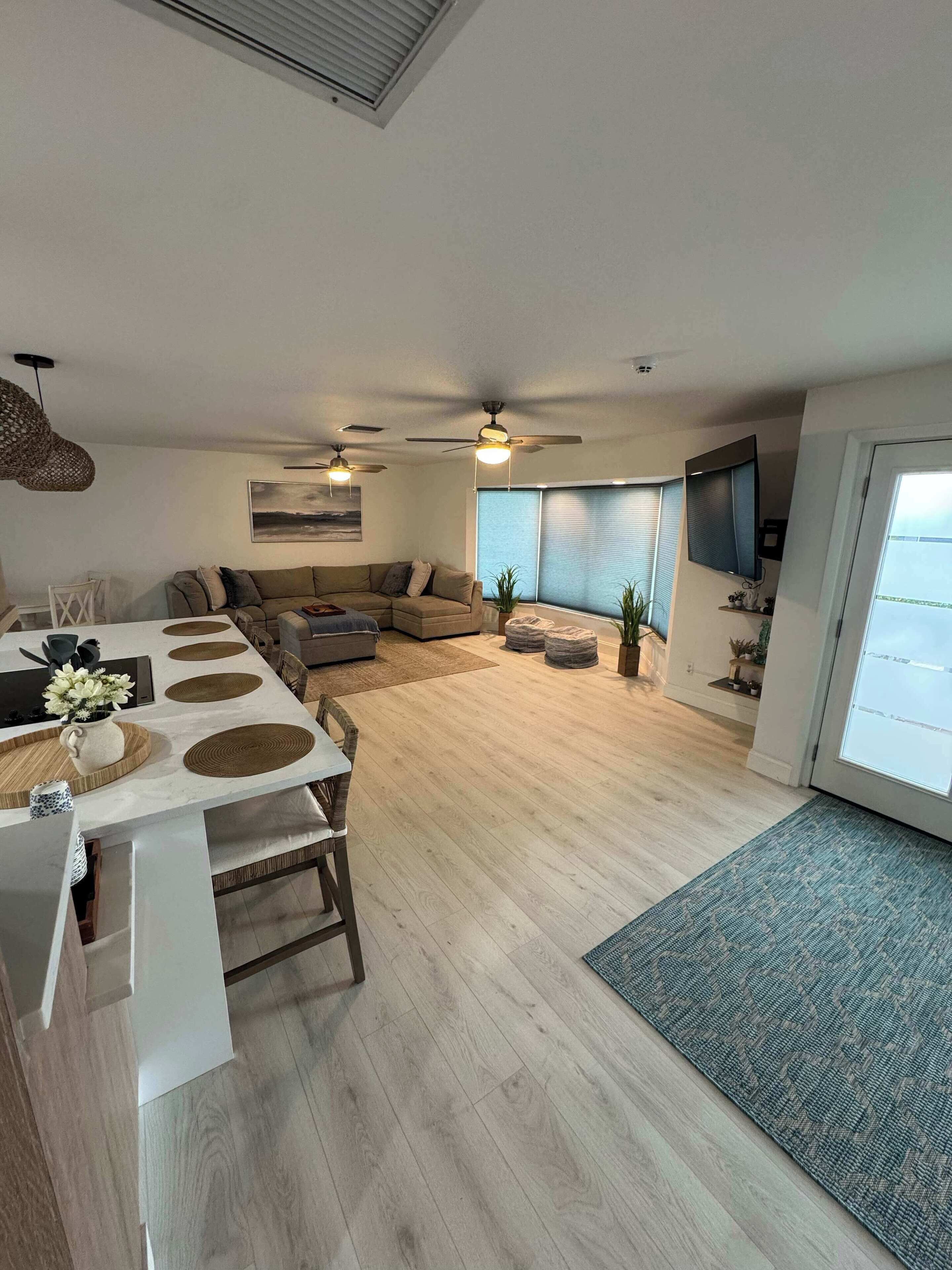 Un salon moderne avec un coin repas, une grande fenêtre et des ventilateurs de plafond.