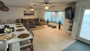 A modern living room with a dining area, a large window, and ceiling fans.