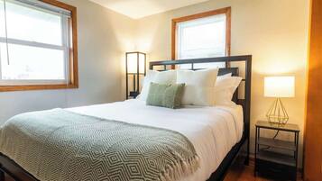 A neatly made bed with a patterned blanket, two bedside lamps, and a nightstand with a geometric lamp.
