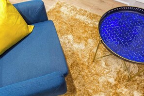 A blue sofa with a yellow pillow, a brown shag rug, and a blue patterned side table. - Childebert - Furnished apartment - Downtown Lyon (Lyon)