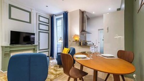 Un salon moderne comprenant un téléviseur, une table à manger avec des chaises, un canapé et un coin cuisine avec une cuisinière et des placards.