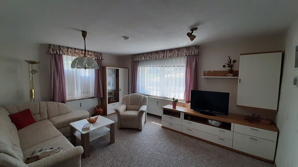 Een woonkamer met een bank, fauteuil, salontafel, televisie en een kast.