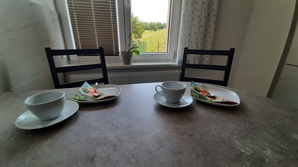 Une table à manger avec quatre tasses et soucoupes blanches, une cuillère et une petite plante en pot.