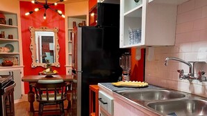 A kitchen with a red accent wall, a black refrigerator, a sink, and a dining area with a table and chairs. - 1BR Coastal Escape (Galveston)
