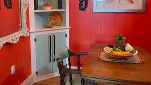 A dining area with a wooden table, chairs, a fruit platter, a decorative mirror, and a ceiling light fixture. - 1BR Coastal Escape (Galveston)