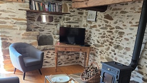 Una sala de estar acogedora con pared de piedra, vigas de madera, televisor, chimenea y muebles modernos.