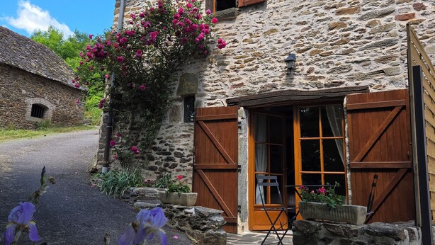 Un edificio de piedra con puerta y contraventanas de madera, una ventana pequeña y un balcón.