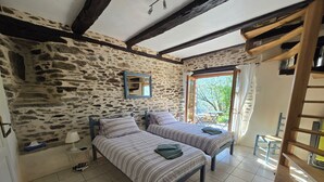 Habitación con dos camas, paredes de piedra, techo de madera y vistas al exterior.