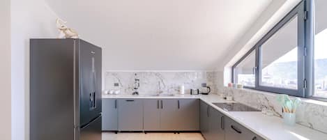 Enjoy a city view from the kitchen window, featuring a stainless steel refrigerator and sleek cabinetry.