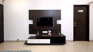 Ein modernes Wohnzimmer mit einem großen Flachbildfernseher an einer dunkelholzverkleideten Wand, einer integrierten Unterhaltungseinrichtung darunter und einer Tür mit einem Hinweisschild.