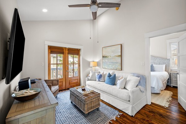 A living room with a white sofa, a television, a wooden coffee table, and a ceiling fan.