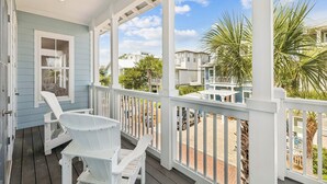 A covered porch with white railings, a table, and two Adirondack chairs.