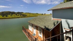 A wooden cabin with a balcony overlooking a calm lake, surrounded by greenery.