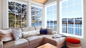 A cozy living room with a large sectional sofa, a wooden coffee table, and a view of a lake through large windows.