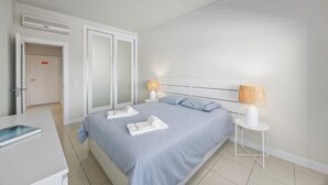 Una habitación de hotel moderna con una cama grande, dos lámparas de noche, una mesita de noche blanca y una puerta con un cartel.