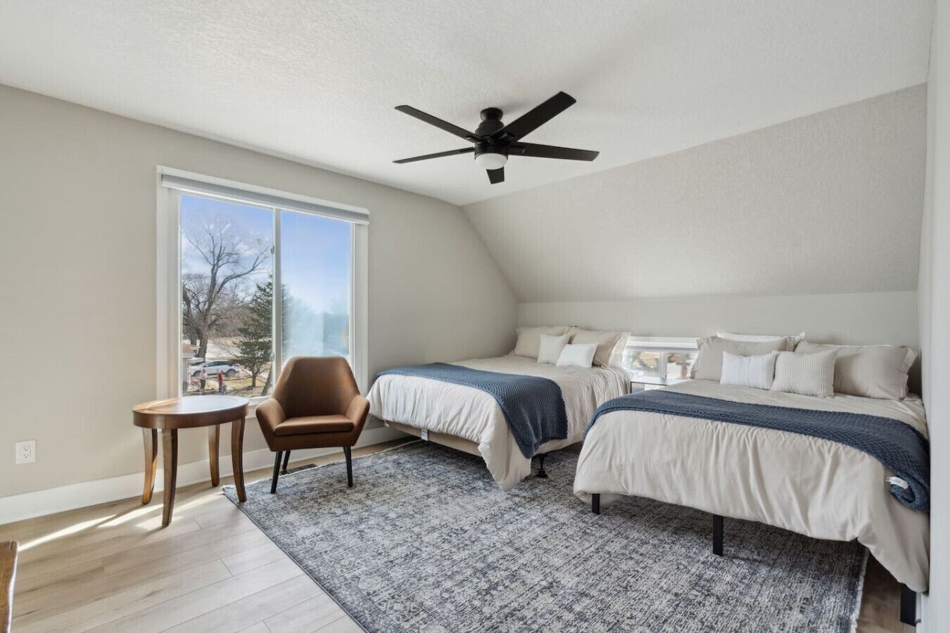 Ein Schlafzimmer mit zwei Betten, einem Deckenventilator, einem Fenster und einem kleinen Tisch.