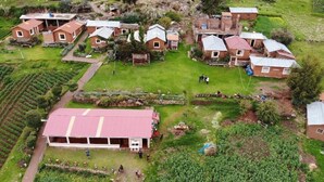 Vue aérienne d’un village rural avec plusieurs petites maisons, un grand bâtiment doté d’un toit rouge et des champs agricoles environnants.
