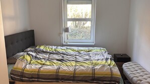 Une chambre à coucher avec un lit, une fenêtre, une table de chevet et un banc.