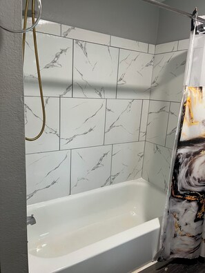 Un baño con bañera, baldosas con diseño de mármol y cortina de ducha.