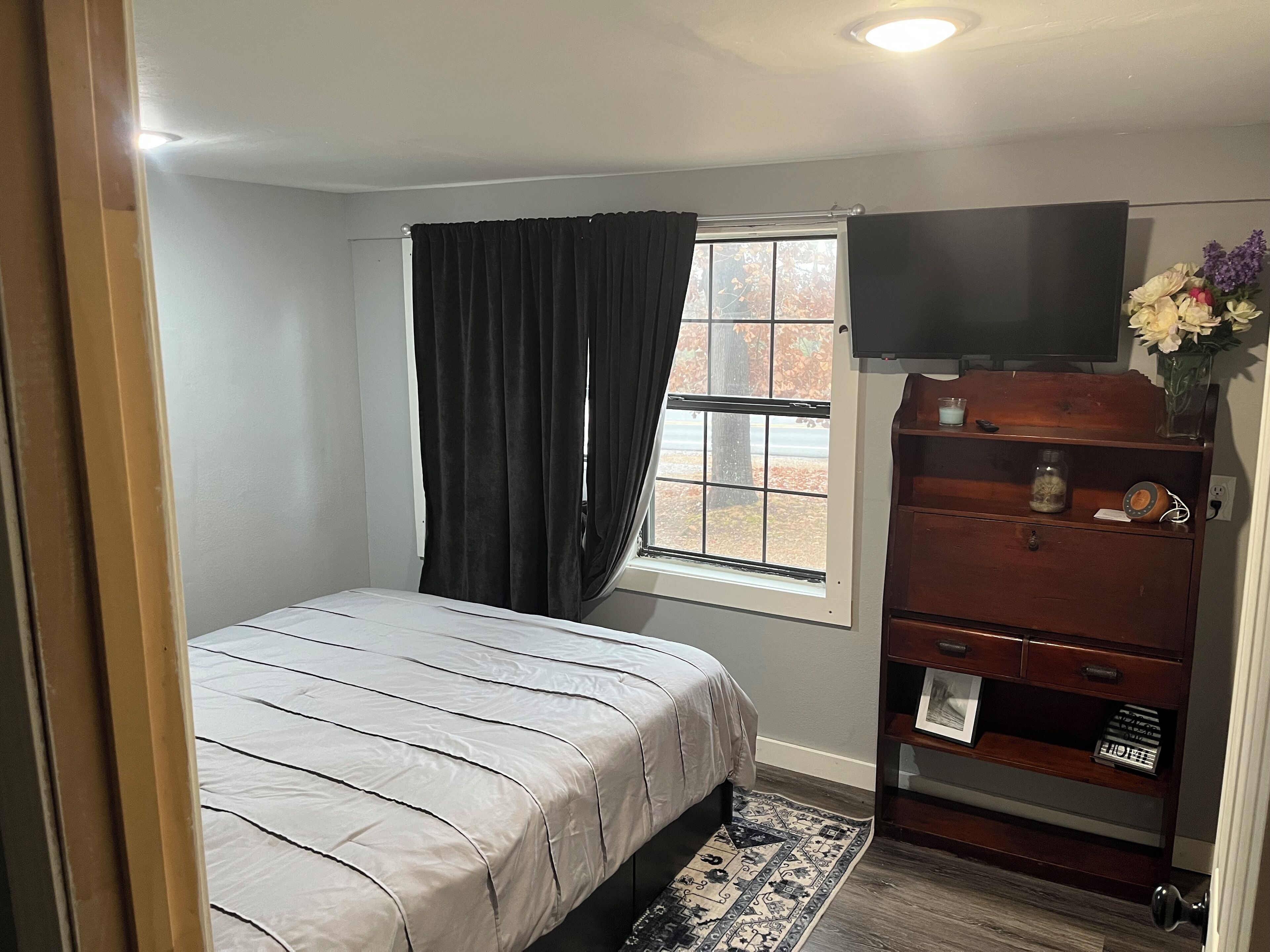 A bedroom with a bed, a dresser, a television, and a window with curtains.