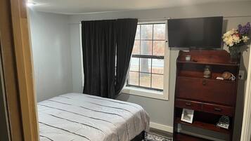 A bedroom with a bed, a dresser, a television, and a window with curtains.