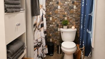 A bathroom with a toilet, a shower curtain, a towel rack, a trash bin, and a recycling bin.