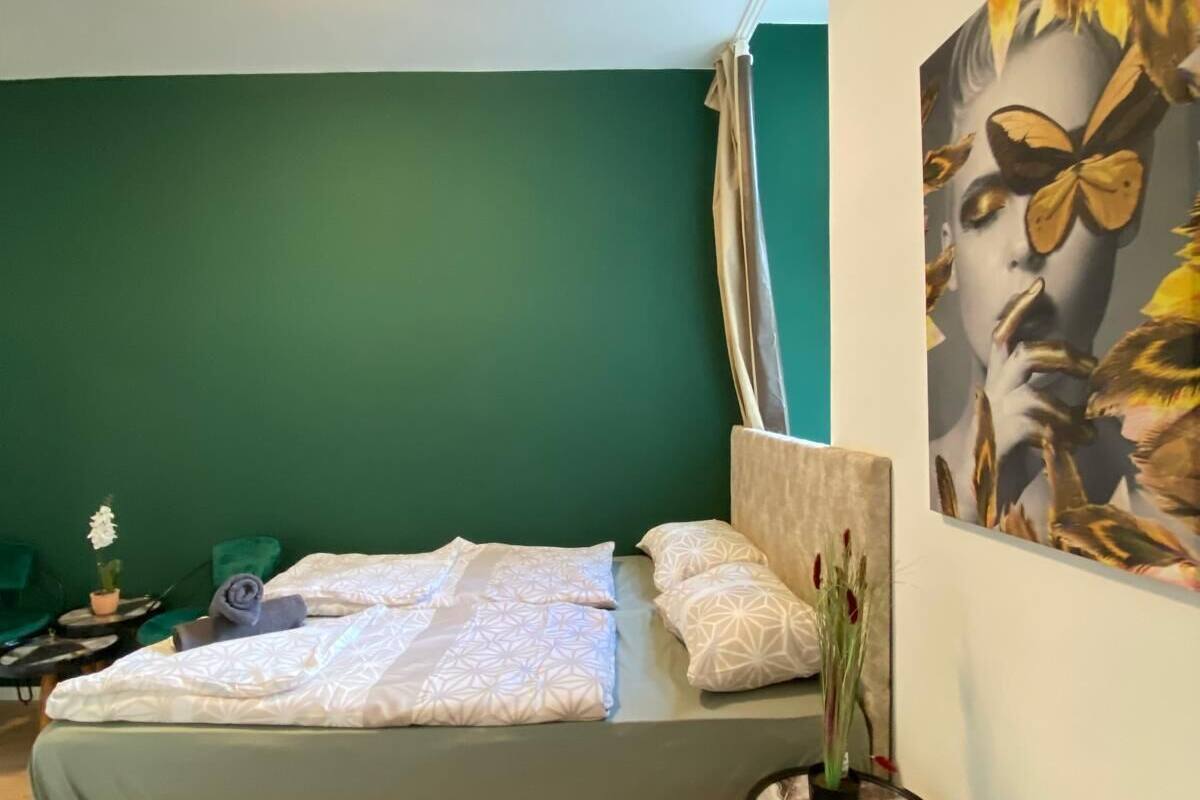 A modern bedroom with a bed, a small table with a vase, and a large painting on the wall.