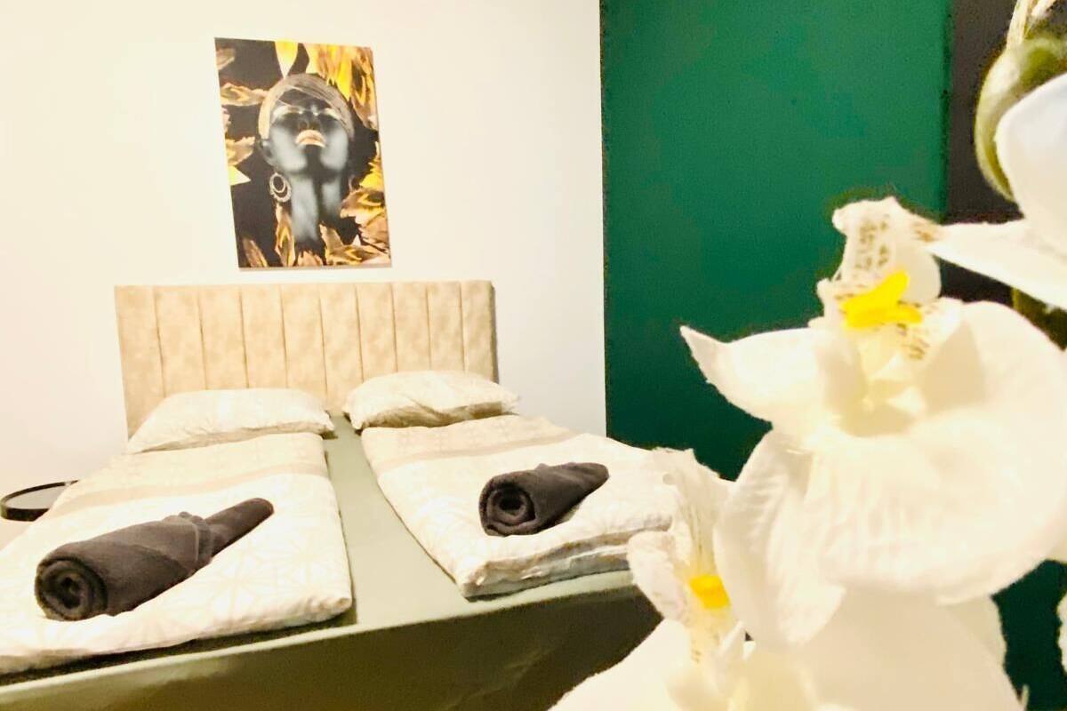 A bedroom with a bed, pillows, a headboard, a painting on the wall, and a white orchid.
