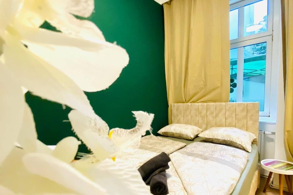 A neatly made bed with a green headboard, a window with curtains, and a small table beside the bed.
