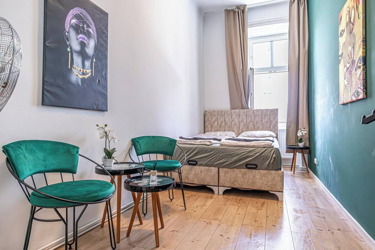A bedroom with a bed, two chairs, a small table, and a window with curtains.