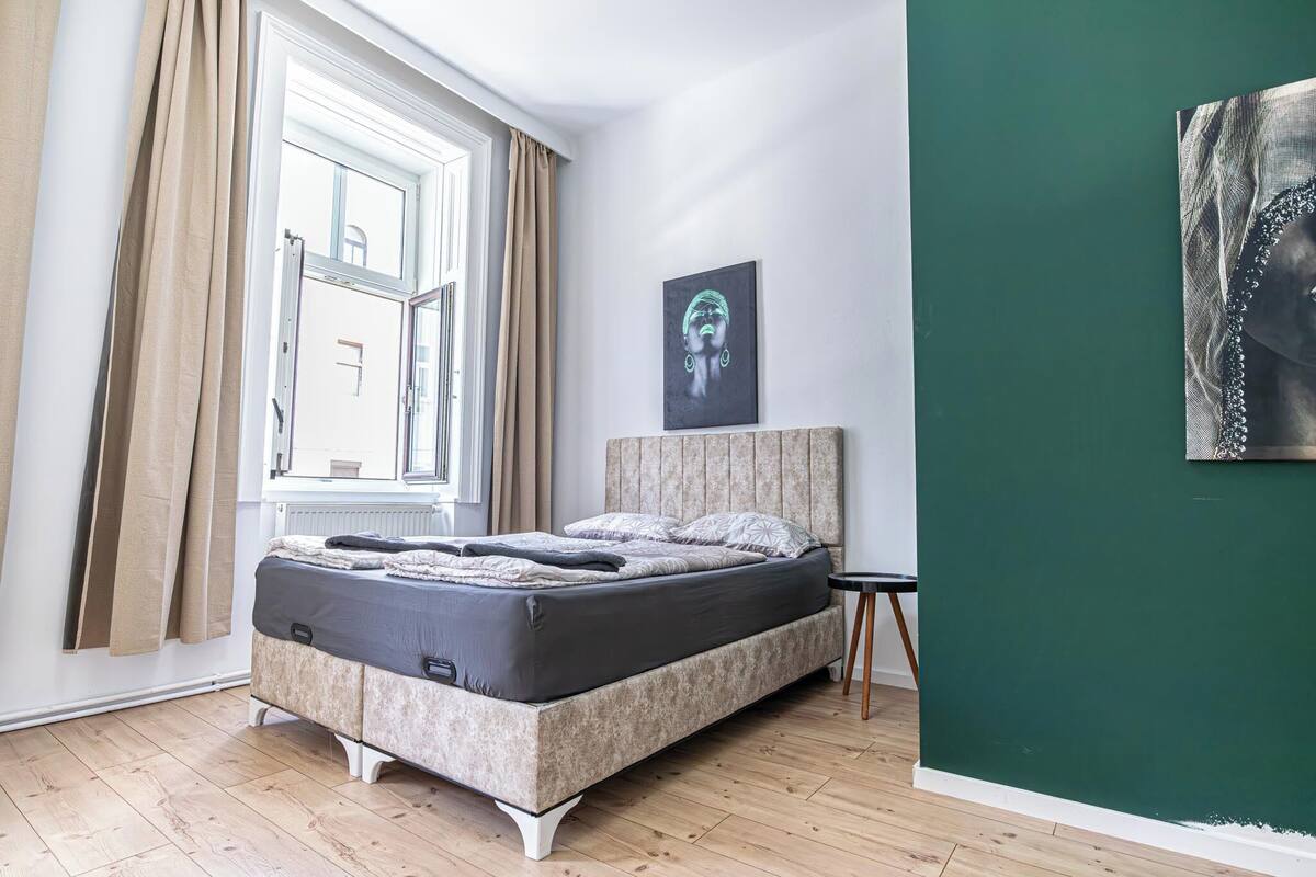 A bedroom with a bed, a window with curtains, a headboard, and a green wall.