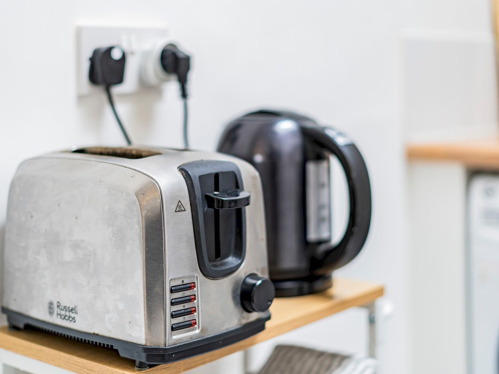 A kitchen with a toaster and a kettle on a wooden shelf.