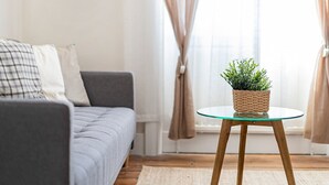 A living room with a grey sofa, a round glass table with a woven basket containing a plant, and a window with curtains. - The Loft - Beautiful flat in Chelsea, London - Pass the Keys (London)