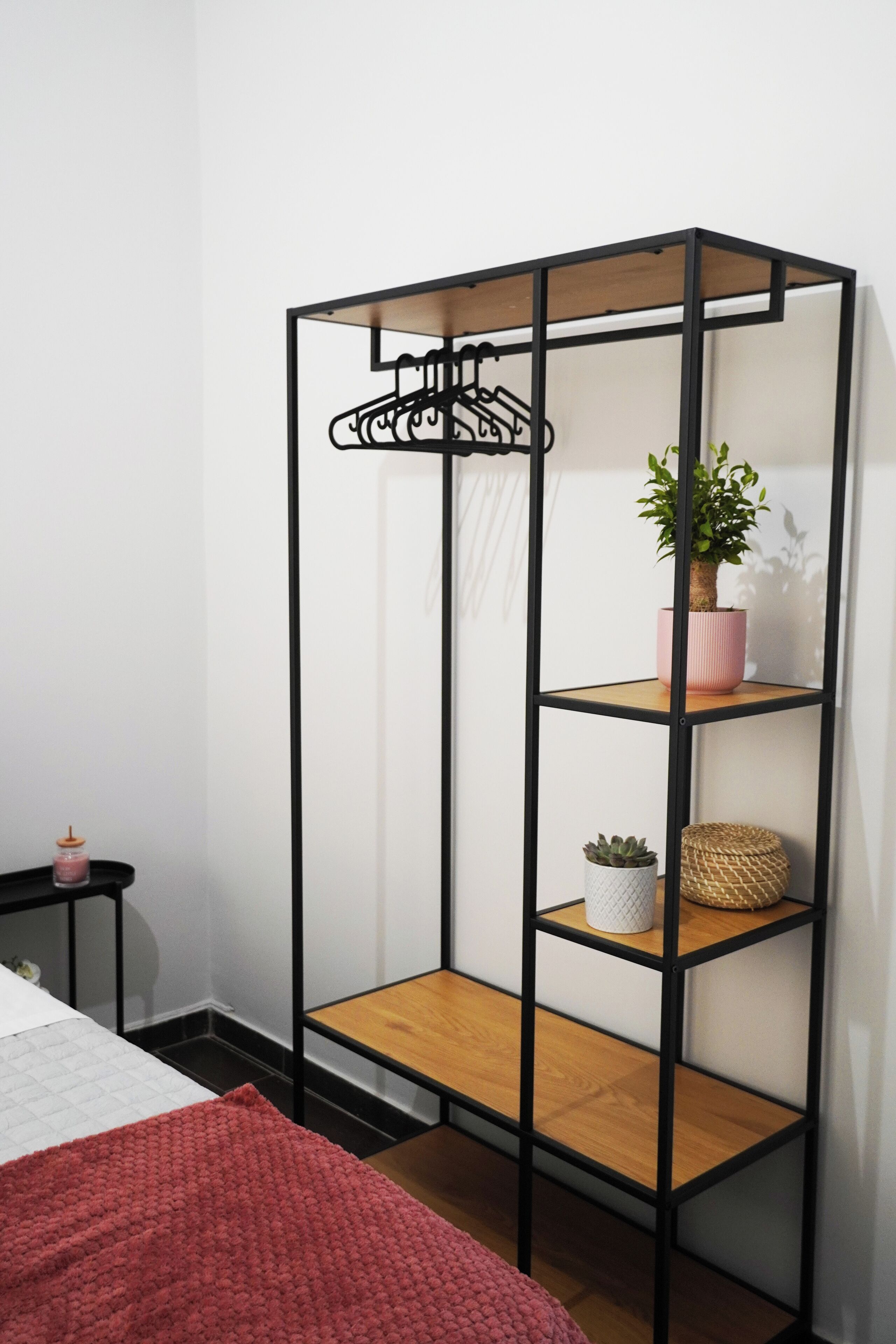 A room with a black metal shelving unit with three shelves, a pink potted plant, and a small white pot on the middle shelf.