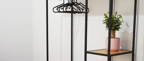 A room with a black metal shelving unit with three shelves, a pink potted plant, and a small white pot on the middle shelf.