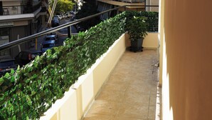 A narrow balcony with a tiled floor, a potted plant, and a view of a street with parked cars and buildings. - Athenian Petralona Suite (Athens)