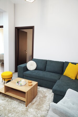 A modern living room with a dark green sofa, a wooden coffee table, and a yellow ottoman. - Athenian Petralona Suite (Athens)