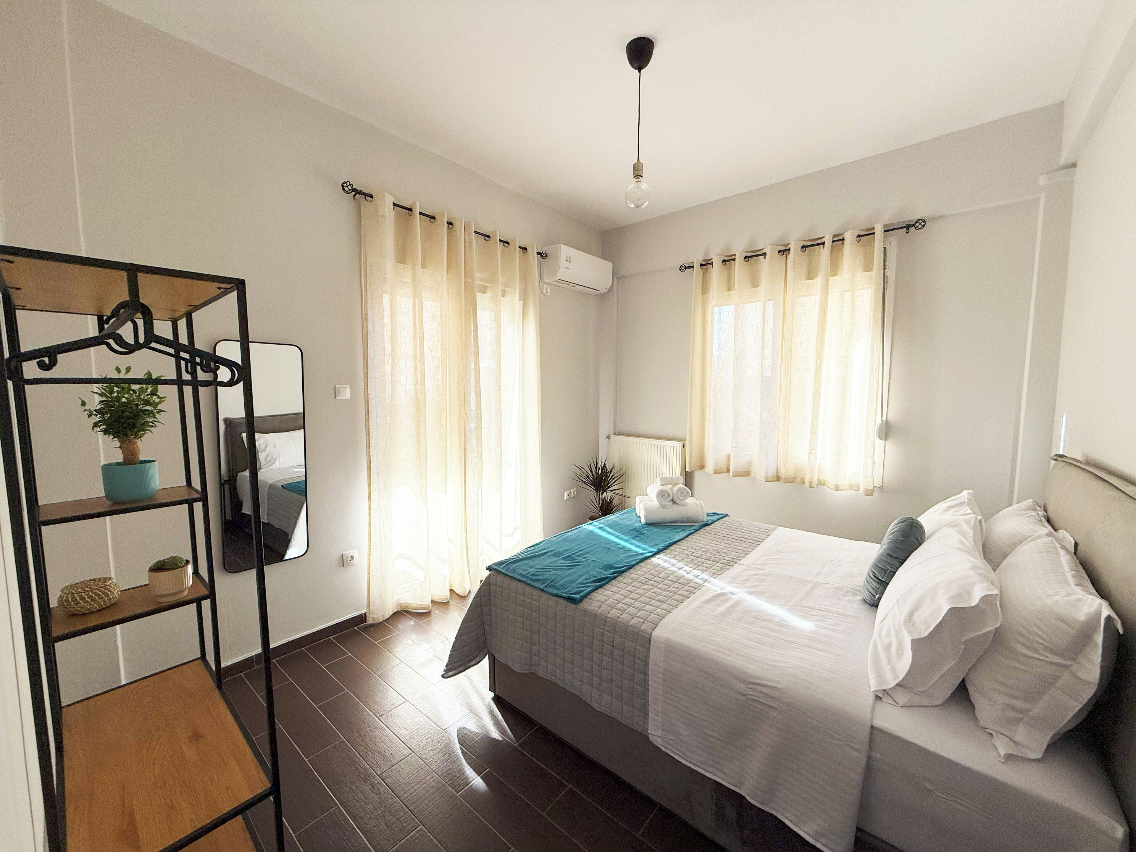 A bedroom with a bed, a bedside table, a hanging plant, and a window with curtains.
