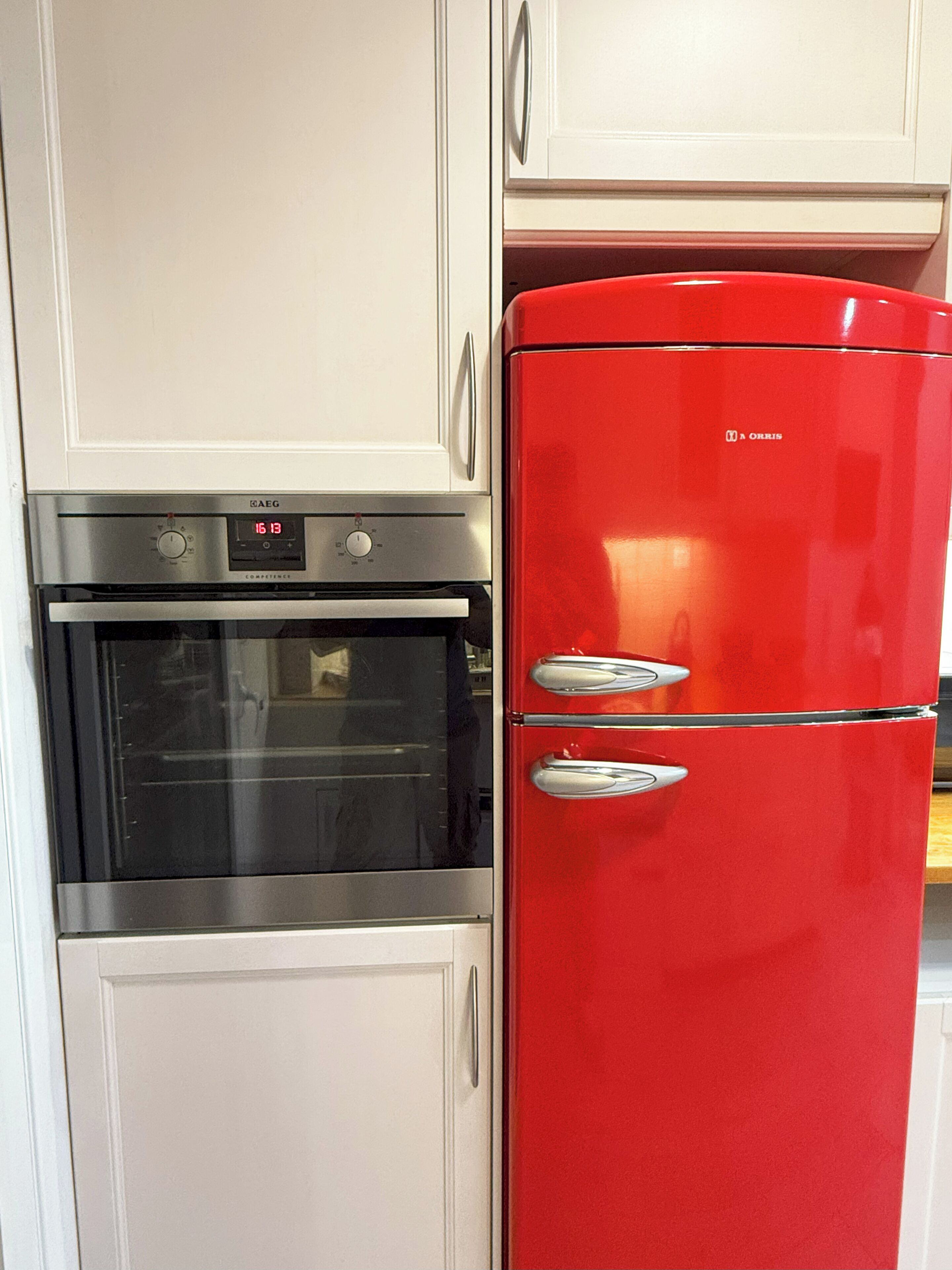 A kitchen with a stainless steel oven and a red refrigerator.
