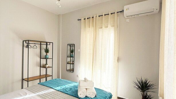 A bedroom with a bed, a bedside table, a mirror, a shelf with plants, and an air conditioning unit. - Athenian Petralona Suite (Athens)