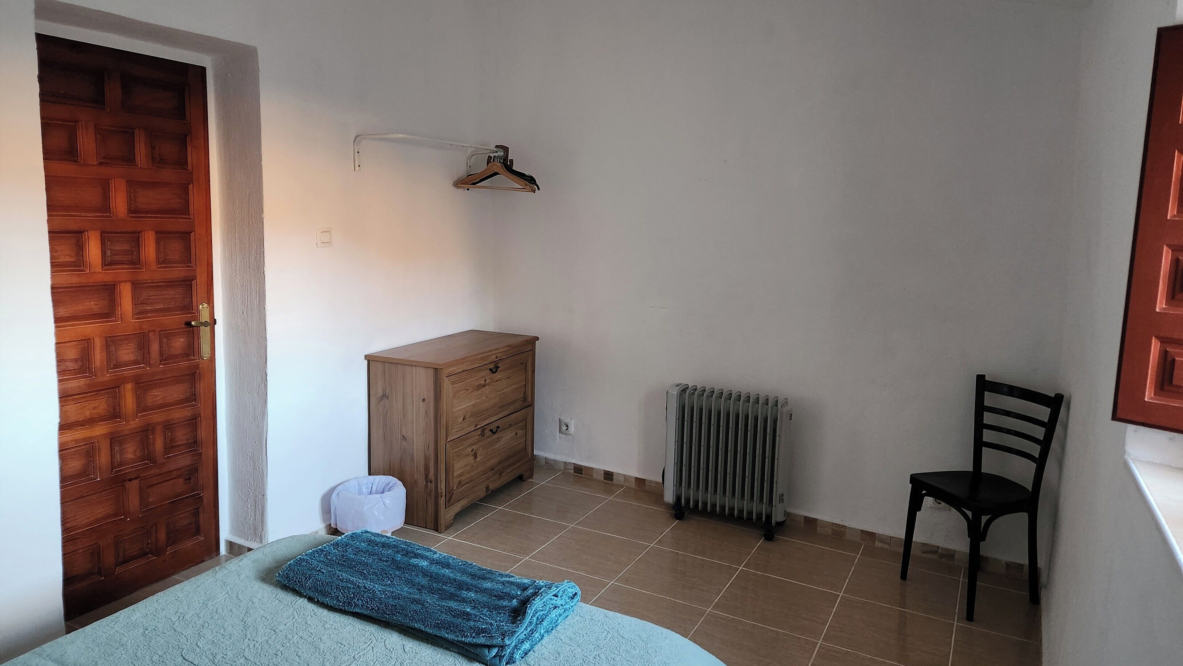 A bedroom with a wooden wardrobe, a radiator, a chair, and a bed with a blue blanket.