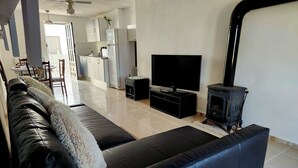 Una sala de estar con un sofá de cuero negro, un televisor de pantalla plana, un mueble de entretenimiento negro y una estufa de leña.