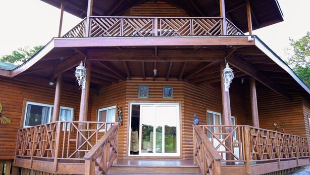 A wooden cabin with a balcony, a staircase leading to the entrance, and a door with glass panels.