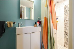 Un baño con un lavamanos blanco, un espejo y una cortina de ducha con un estampado colorido.