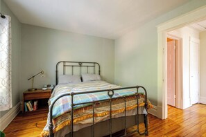 Un dormitorio con estructura de cama metálica, una mesita de noche con lámpara, una estantería y una puerta que da a otra habitación.