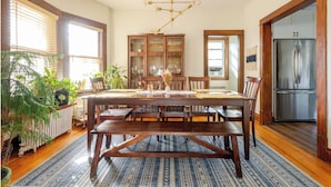 A dining room with a wooden table, chairs, a chandelier, and a refrigerator.