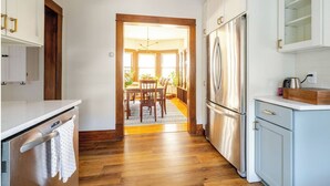 A kitchen with wooden flooring, white cabinets, a stainless steel refrigerator, and a dining area with a table and chairs.